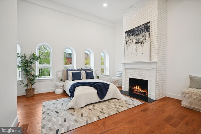 bedroom with brick wall, a high ceiling, dark wood-type flooring, and a fireplace