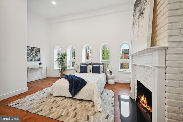 bedroom featuring a towering ceiling, brick wall, a fireplace, and dark wood-type flooring