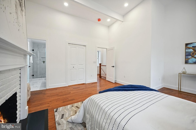 bedroom featuring dark hardwood / wood-style flooring, ensuite bath, beamed ceiling, and a fireplace