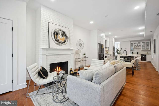 living room featuring a brick fireplace, dark wood-type flooring, brick wall, and sink