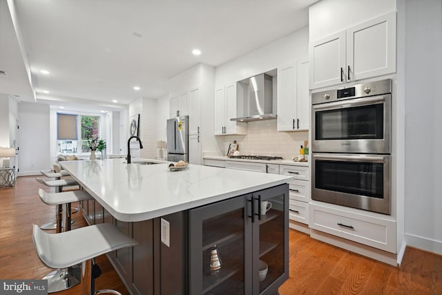 kitchen featuring light hardwood / wood-style floors, white cabinets, wine cooler, stainless steel appliances, and wall chimney exhaust hood