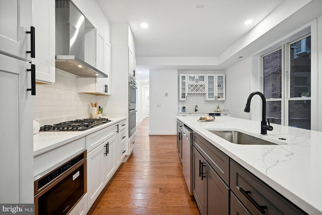 kitchen with sink, light stone counters, white cabinets, light hardwood / wood-style floors, and wall chimney range hood