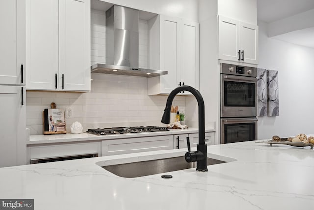 kitchen featuring light stone counters, white cabinets, appliances with stainless steel finishes, backsplash, and wall chimney range hood