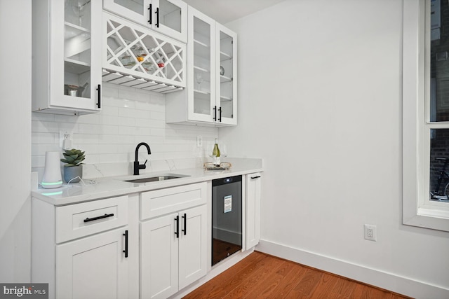 bar featuring dark wood-type flooring, white cabinetry, light stone countertops, backsplash, and sink