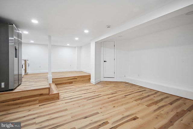 basement with light wood-type flooring and stainless steel refrigerator with ice dispenser