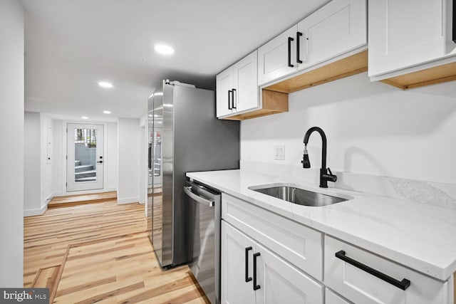 kitchen featuring light hardwood / wood-style floors, white cabinets, stainless steel dishwasher, light stone countertops, and sink