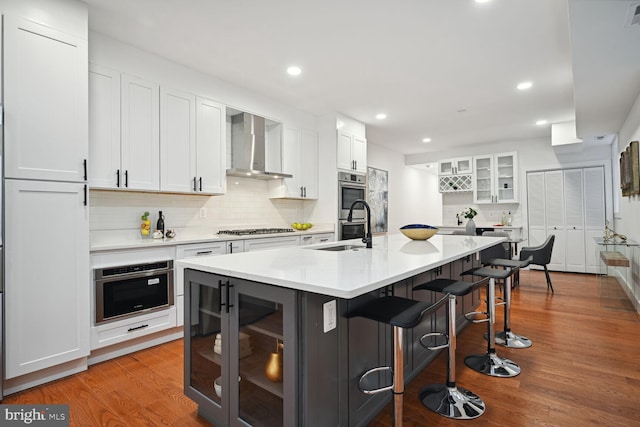 kitchen featuring white cabinetry, light hardwood / wood-style floors, appliances with stainless steel finishes, and wall chimney range hood