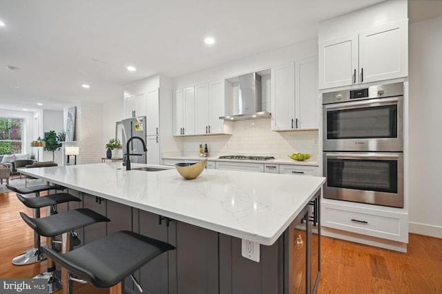 kitchen with white cabinets, appliances with stainless steel finishes, light hardwood / wood-style flooring, backsplash, and wall chimney range hood