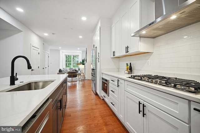 kitchen with sink, white cabinets, backsplash, wood-type flooring, and wall chimney range hood