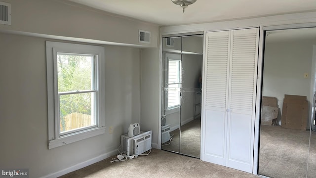 unfurnished bedroom with multiple closets, light colored carpet, and a wall mounted air conditioner