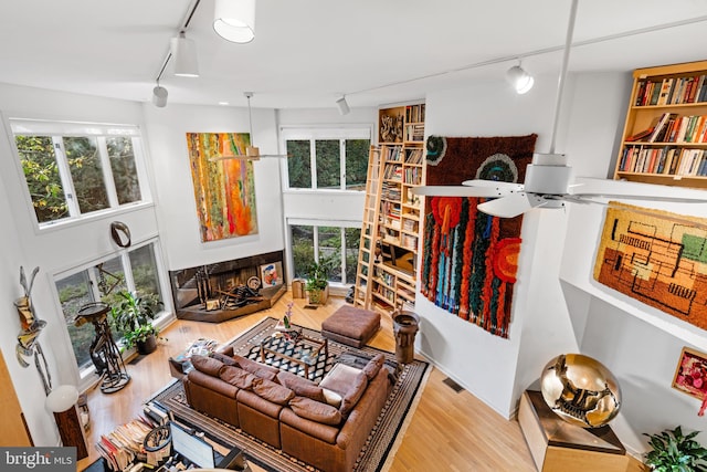 living room featuring rail lighting, light hardwood / wood-style flooring, ceiling fan, and a high ceiling