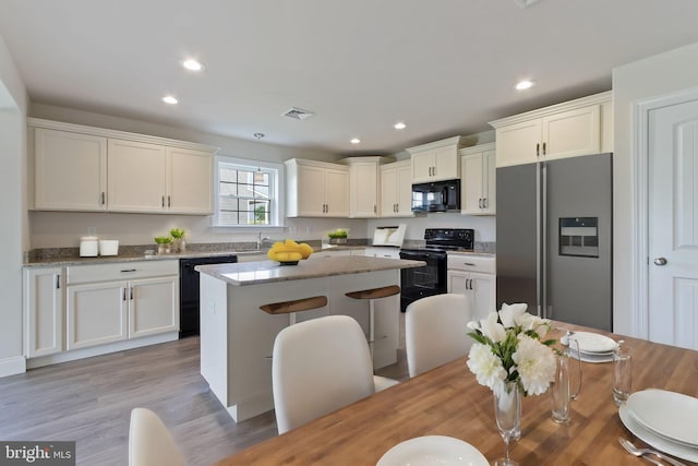 kitchen with light stone counters, light hardwood / wood-style floors, a breakfast bar, a kitchen island, and black appliances