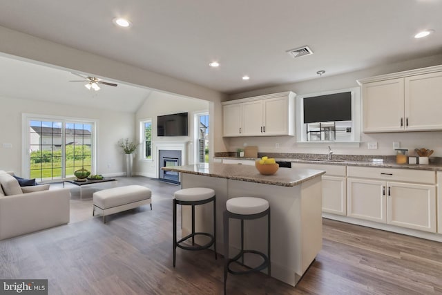 kitchen with a center island, dark stone counters, vaulted ceiling, white cabinetry, and wood-type flooring