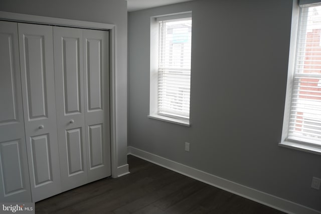 unfurnished bedroom with dark hardwood / wood-style flooring, a closet, and multiple windows