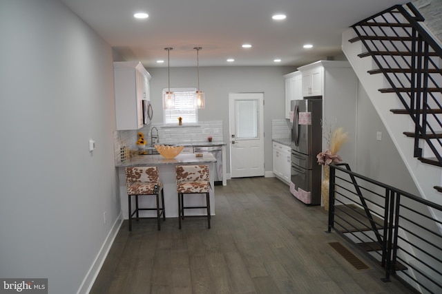 kitchen with decorative light fixtures, dark wood-type flooring, appliances with stainless steel finishes, white cabinets, and backsplash