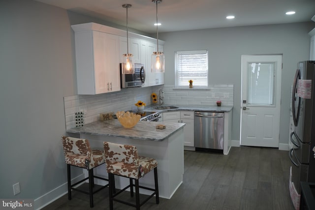 kitchen featuring decorative light fixtures, appliances with stainless steel finishes, a kitchen bar, white cabinets, and dark hardwood / wood-style flooring