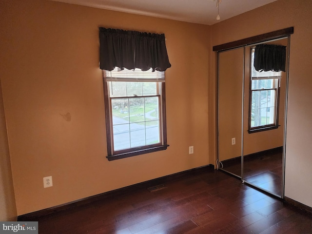 unfurnished bedroom with a closet, dark wood-type flooring, and multiple windows