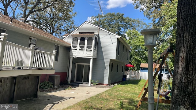 rear view of property with central AC, a balcony, a patio, and a lawn