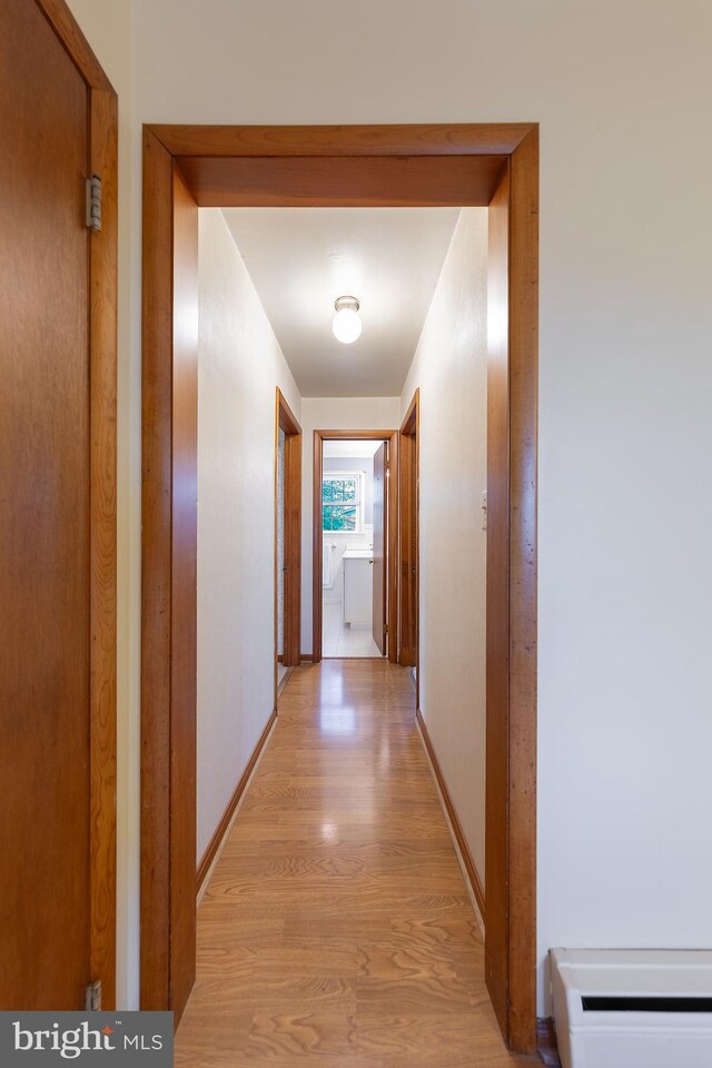 corridor featuring baseboards, light wood finished floors, and a baseboard heating unit