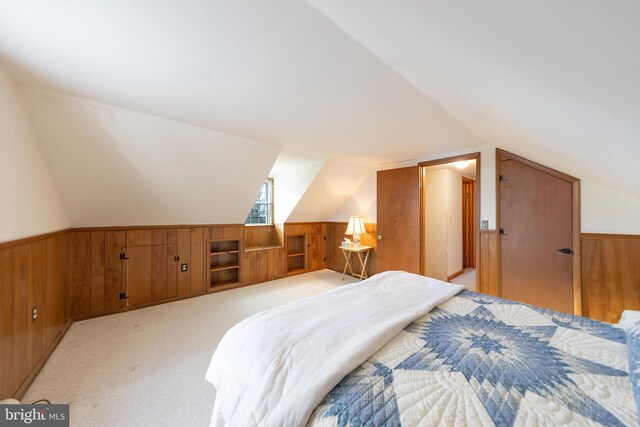 bedroom featuring wooden walls, vaulted ceiling, wainscoting, and light carpet