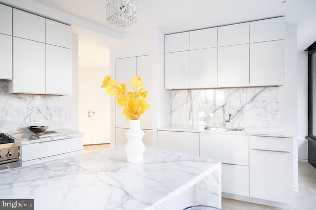 kitchen featuring a notable chandelier, white cabinetry, sink, and gas range