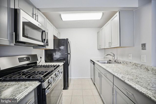 kitchen with appliances with stainless steel finishes, light stone counters, gray cabinetry, light tile floors, and sink