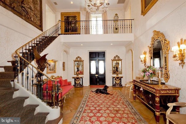 foyer featuring ornamental molding, a high ceiling, light parquet floors, and an inviting chandelier