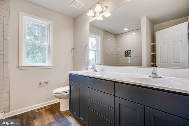 bathroom with wood-type flooring, a tile shower, vanity, and toilet