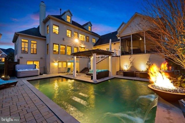 back house at dusk with a patio, a pergola, a fire pit, and a pool with hot tub