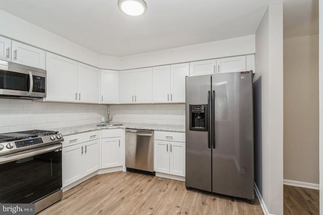 kitchen featuring light stone countertops, tasteful backsplash, appliances with stainless steel finishes, white cabinetry, and light wood-type flooring