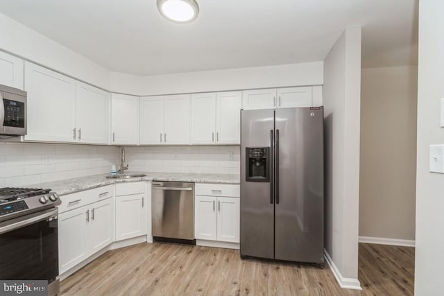 kitchen featuring appliances with stainless steel finishes, sink, light hardwood / wood-style flooring, white cabinets, and tasteful backsplash