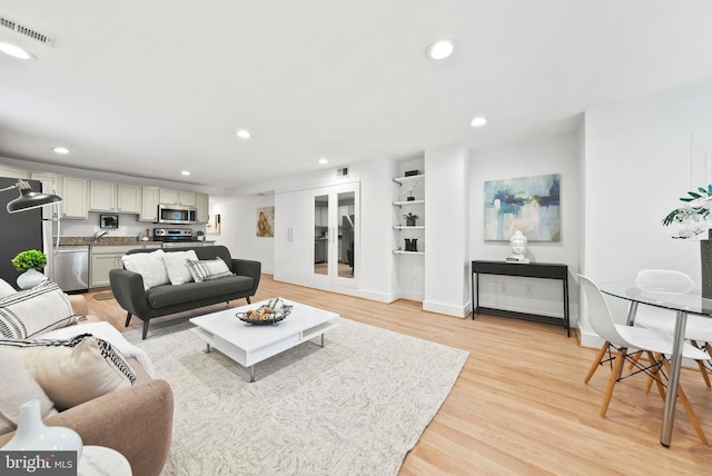 living room featuring french doors, sink, and light hardwood / wood-style floors