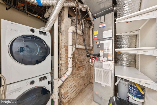 clothes washing area with brick wall and stacked washer and clothes dryer