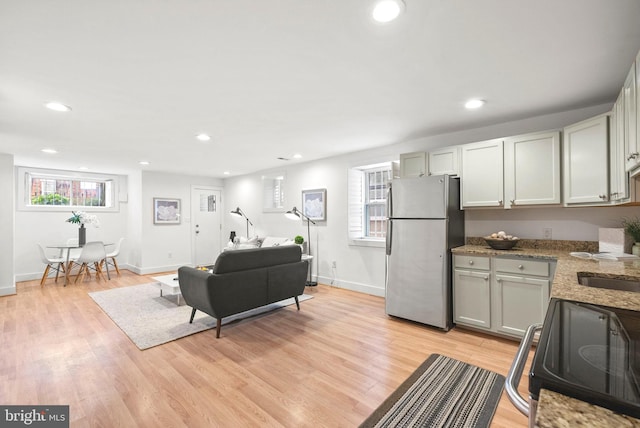 kitchen with stainless steel refrigerator, range, light wood-type flooring, and light stone countertops