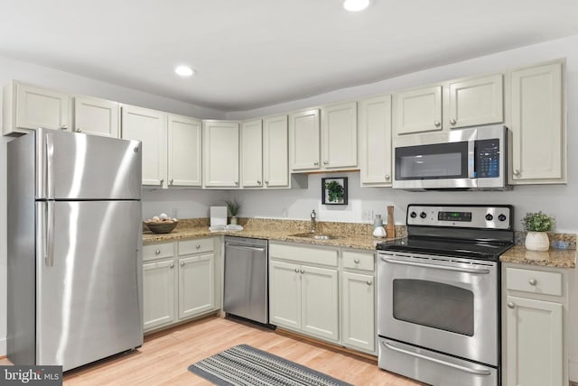 kitchen with appliances with stainless steel finishes, light stone countertops, sink, and light hardwood / wood-style flooring