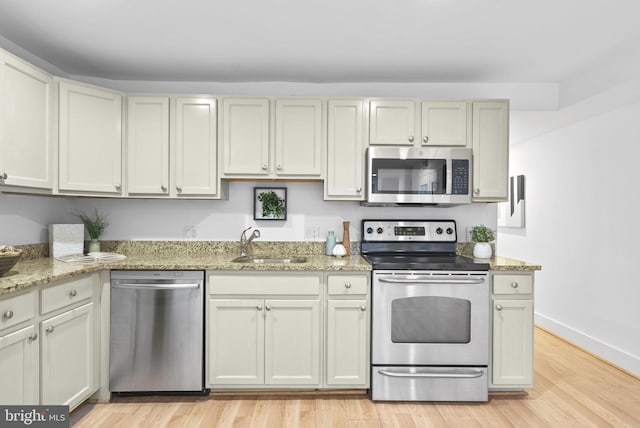 kitchen featuring sink, stainless steel appliances, light wood-type flooring, and light stone counters