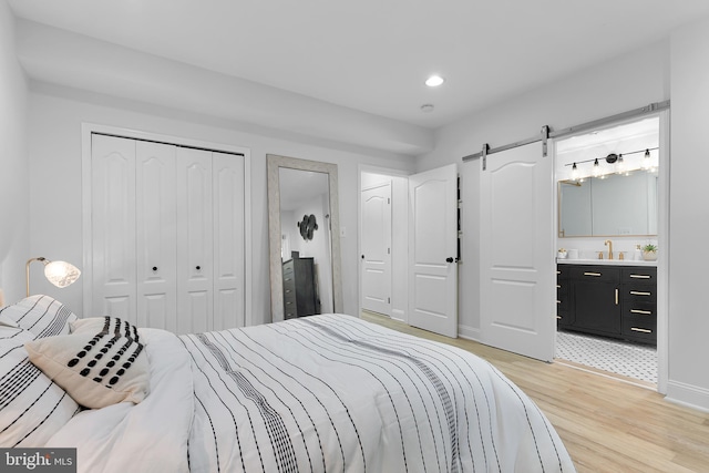 bedroom featuring sink, a barn door, light wood-type flooring, connected bathroom, and a closet