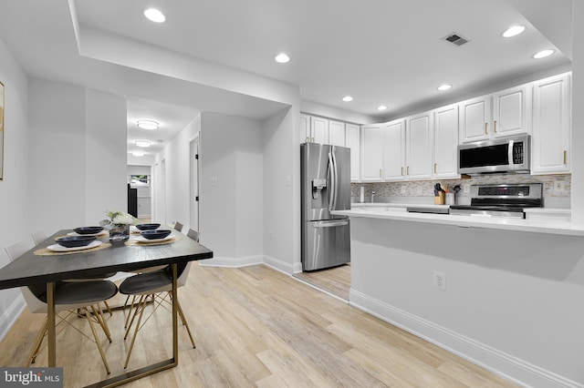 kitchen with white cabinetry, backsplash, appliances with stainless steel finishes, and light hardwood / wood-style flooring