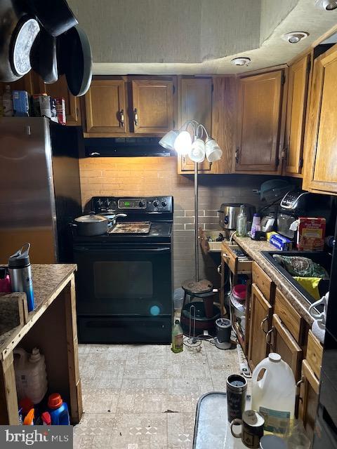 kitchen featuring light tile floors, sink, black / electric stove, tasteful backsplash, and stainless steel fridge