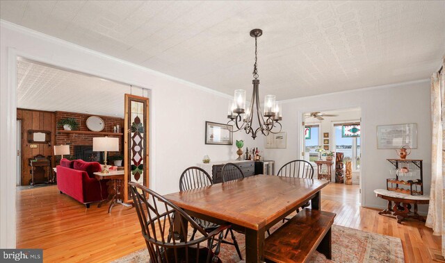 dining area with brick wall, a brick fireplace, ceiling fan with notable chandelier, and light hardwood / wood-style flooring