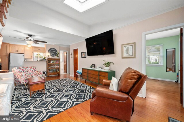 living room featuring ceiling fan, light wood-type flooring, ornamental molding, and a skylight