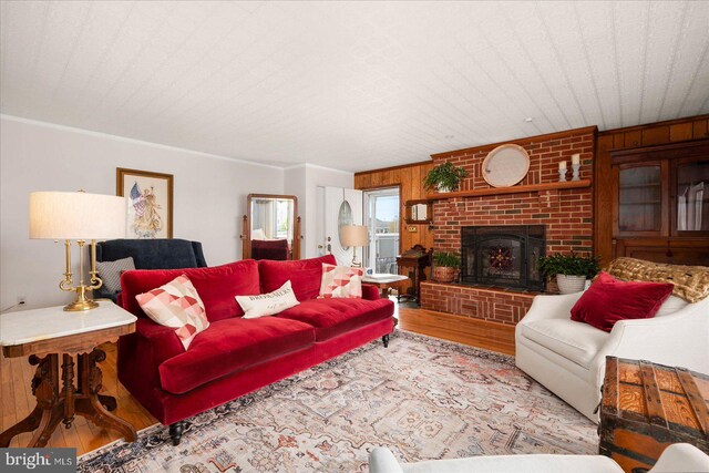 living room with light wood-type flooring, ornamental molding, and a brick fireplace