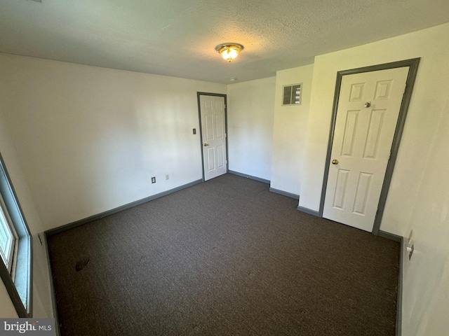 unfurnished room featuring dark carpet and a textured ceiling