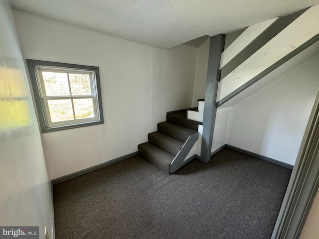 stairway with a textured ceiling and dark colored carpet