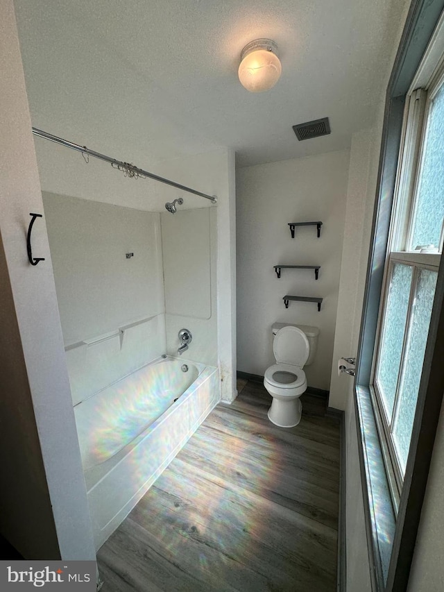 bathroom with wood-type flooring, a textured ceiling, bathtub / shower combination, and toilet