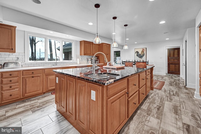 kitchen featuring sink, dark stone counters, decorative light fixtures, and a kitchen island with sink