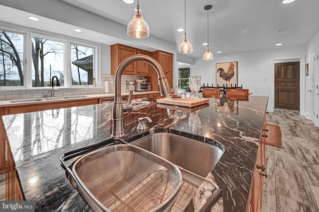 kitchen featuring sink, a kitchen island, decorative light fixtures, and dark stone countertops