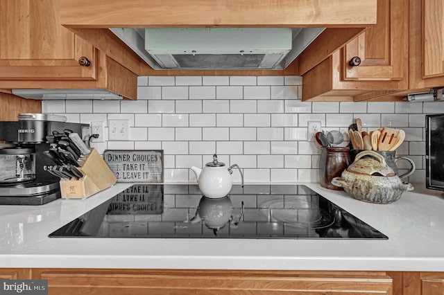 interior details featuring exhaust hood, black electric cooktop, and tasteful backsplash