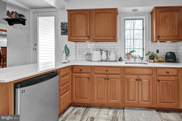 kitchen with kitchen peninsula, tasteful backsplash, stainless steel refrigerator, light hardwood / wood-style flooring, and sink