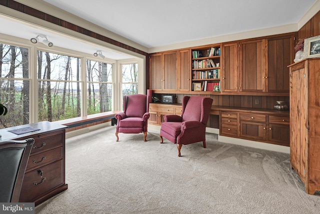 sitting room with built in desk, wooden walls, crown molding, and light colored carpet